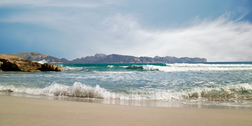 Waves gently roll onto the sandy shore at Canggu Beach, with mountains in the distance.