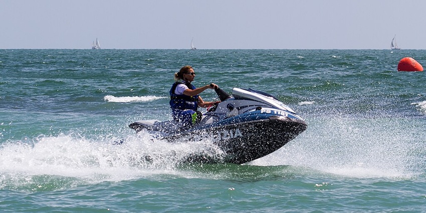 A man on his Jet Ski splashes water with a backdrop of glittery water in the sea.