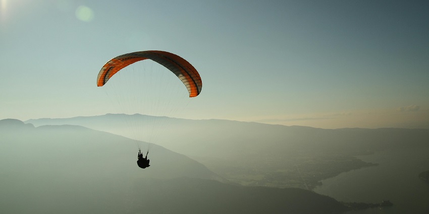 Paragliding in Panchgani, with an orange canopy against a hazy sky, mountainous landscape below