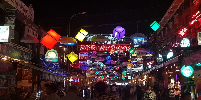 An image of Siem Reap Pub Street in Cambodia, with bright signs and people walking around.