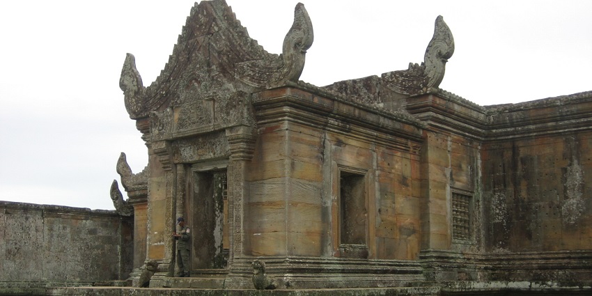 An image of the Preah Vihear with intricate carvings, scattered stones, and a person nearby.