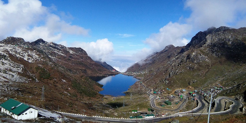 The landscape of Tsomgo Lake with a still water body and the mountains covered in mist.