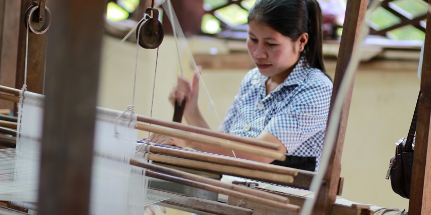 Image of a person using a traditional loom, skillfully weaving fabric with intricate precision in the Angkor Silk Farm.