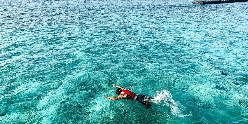 A view of a person snorkelling on the turquoise blue waters through the gushing waves.