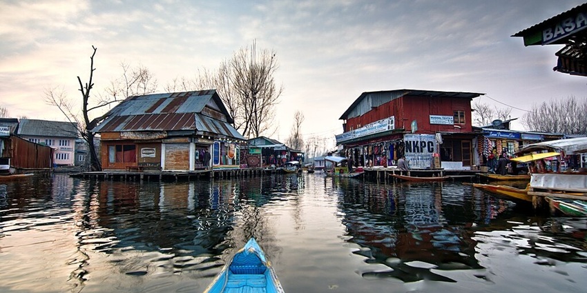 Floating market on Dal Lake with multiple shops, a blue boat and dried trees all around