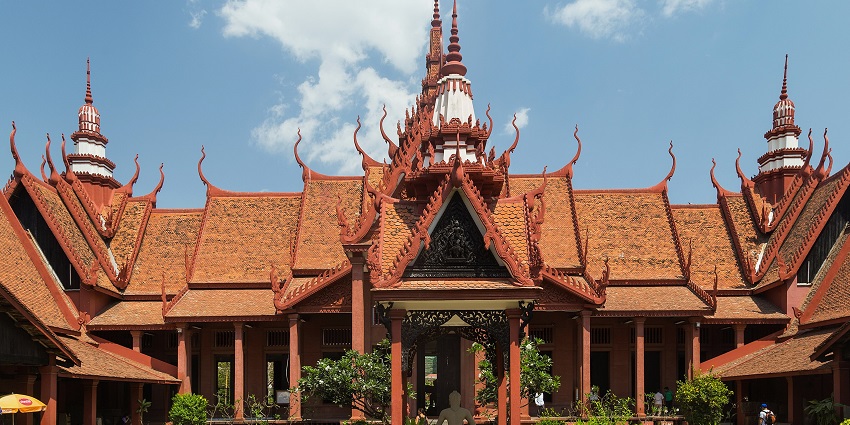 An image of the traditional National Museum of Cambodia building with red ornate roofs, under the clear skies.