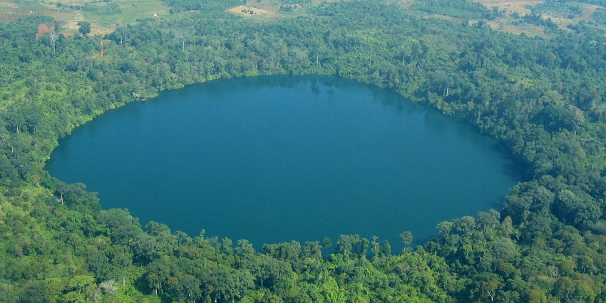 An image of a circular lake encircled by dense forest, with nearby agricultural fields and contrasts visible.