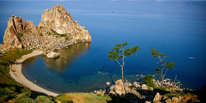 Olkhon island with big rocks in the lake, sandy shorelines and green trees on the island.