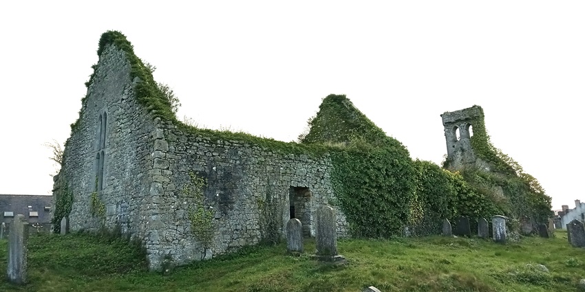 A medieval church made of stones stands erect as green foliage climbs over it.
