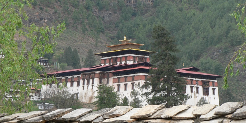 An image of a Dzong in Paro, resembling the Dobji Dzong, with a multi-tiered roof, surrounded by greenery and mountains