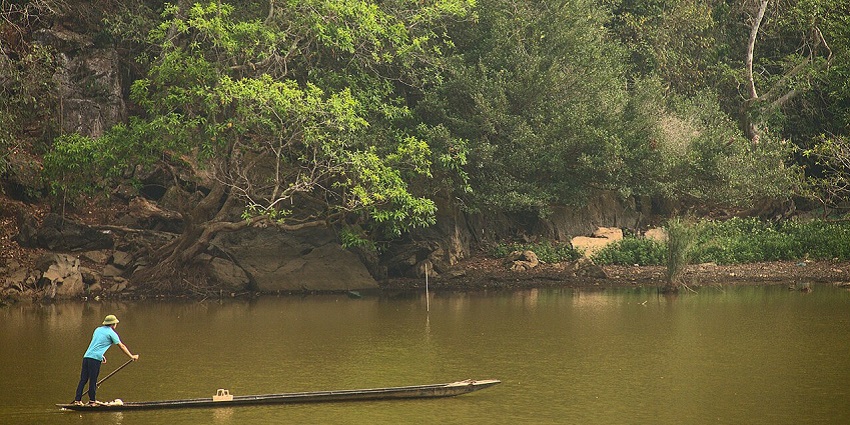 A traditional wooden boat cruising through Ba Be Lake, surrounded by towering cliffs