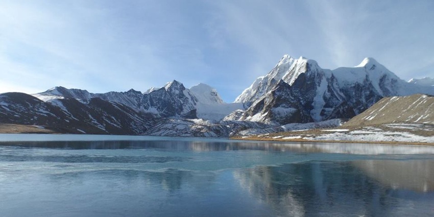 Panoramic view of frozen Gurudongmar Lake in December amidst snow-clad mountains.