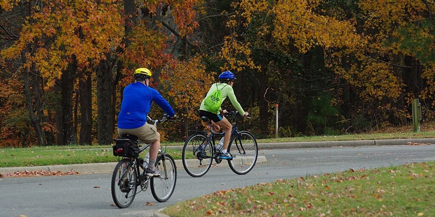 An image of two people with their safety gears on, riding their bikes on a road in a park.