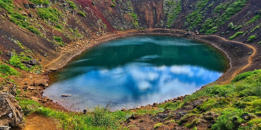Meteor crater lake site with a green and small water body surrounded by mountains