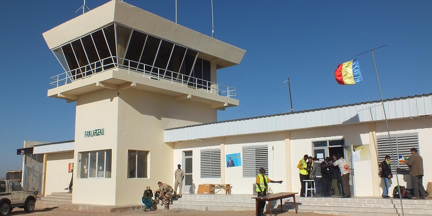 Terminal of Faya Largeau airport with passengers entering the airport and a tall flag