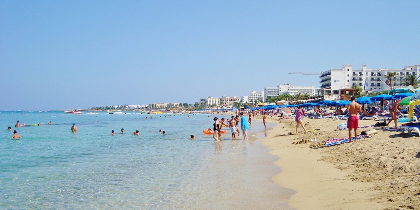 Sandy beach with turquoise water in Cyprus, featuring sun chairs and umbrellas.