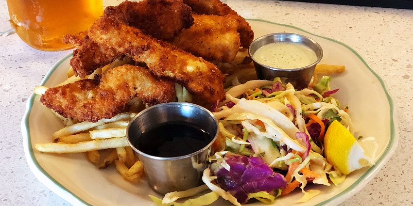 Fish and chips with deep-fried golden brown fish, fries and salad, served with sauces