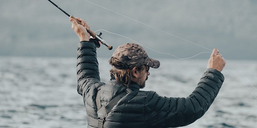 Person fishing while holding a fishing rod and its strings with the lake in the background