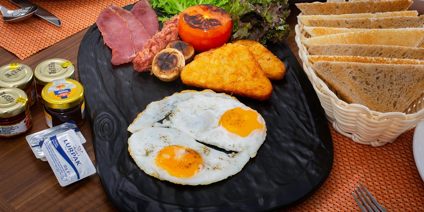A breakfast platter is displaying fried eggs, hash browns, bacon, toast, and fresh greens