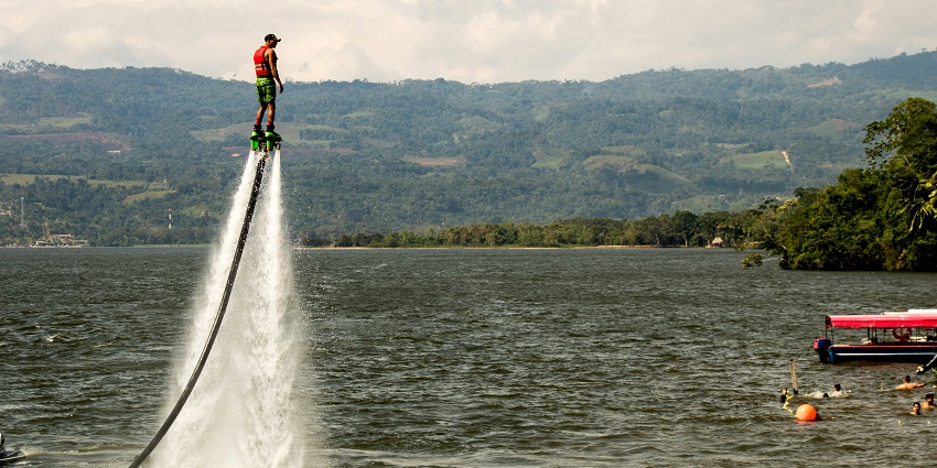 An image of a person flyboarding above the sea, surrounded by boats and bright sunlight.