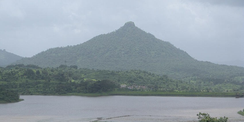 Gadeshwar Reservoir surrounded by greenery and a big mountain in the background