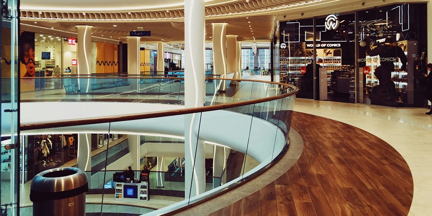 Inside view of a modern shopping mall with lush green potted trees and a spacious walkway