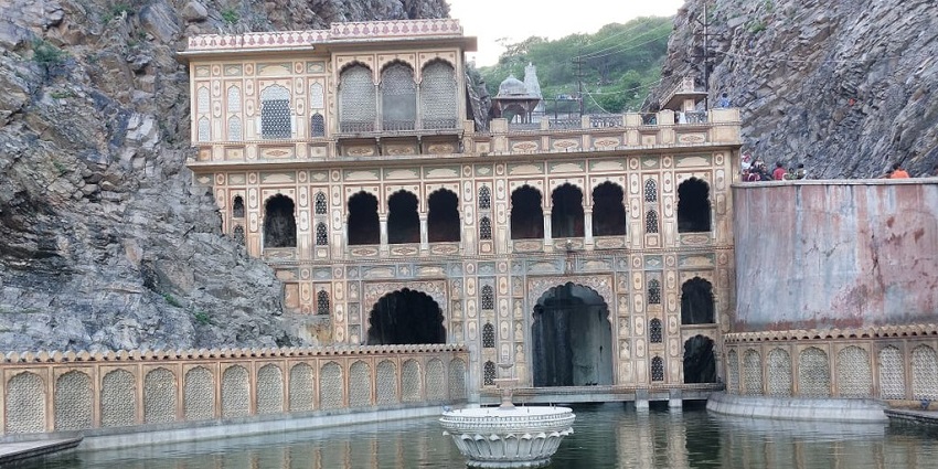 An image of Galta Kund, a sacred water tank in Jaipur, surrounded by ancient temples and hills