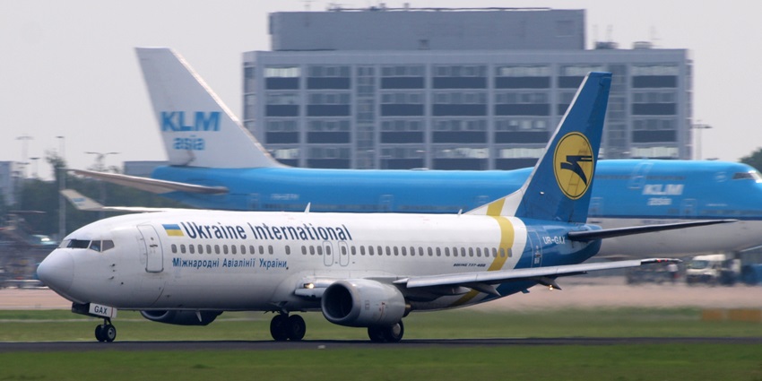 Couple of commercial aeroplanes on the runway with airport buildings in the background