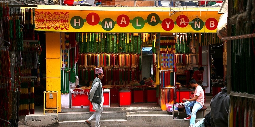Man passing by a shop with its signboard and another man sitting outside the store.