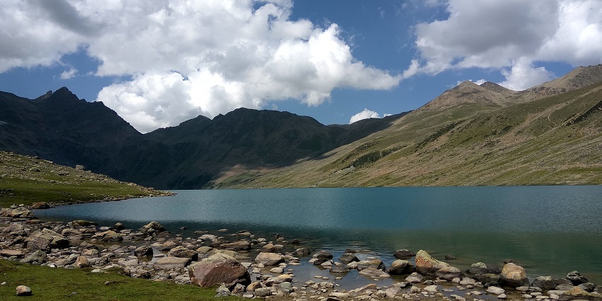 Gangabal lake with a large water body, rocks on the shore and surrounded by mountains