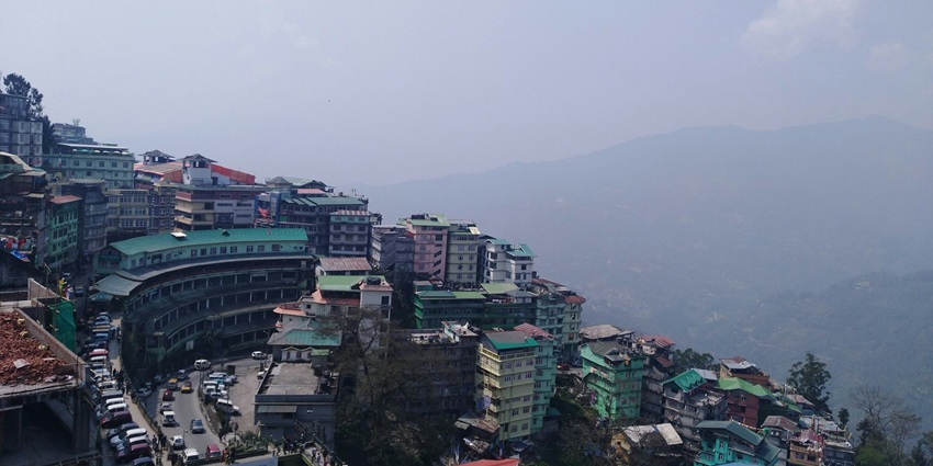 An image of a hilly town of Gangtok, with dense greenery, scattered houses, and a tall communication tower amidst mountains.