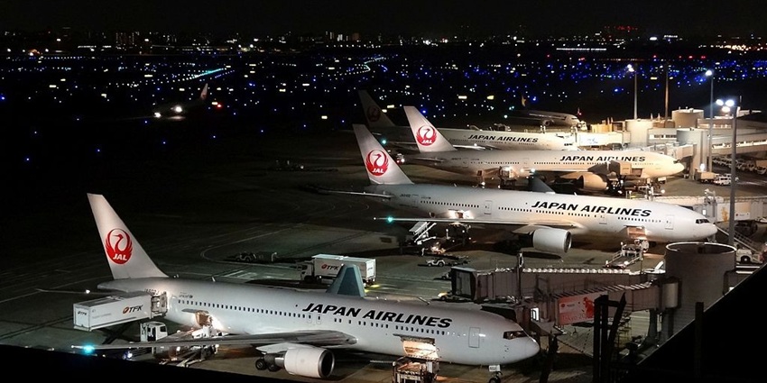 A night sky with a fleet of aircraft along with the aerobridge on a runway.