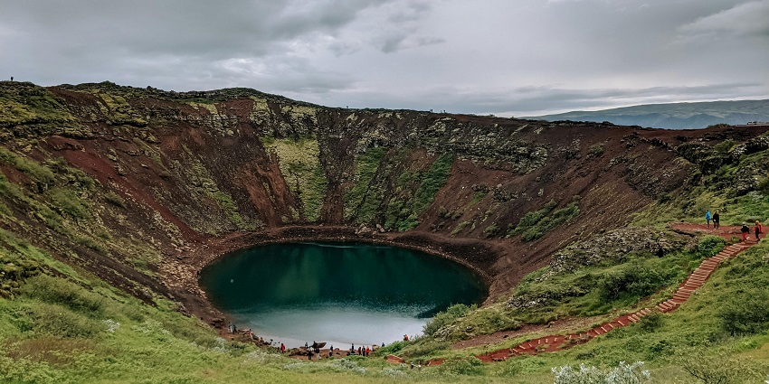 Crater lake site with a green water body surrounded by sandy shorelines and trekking stairs