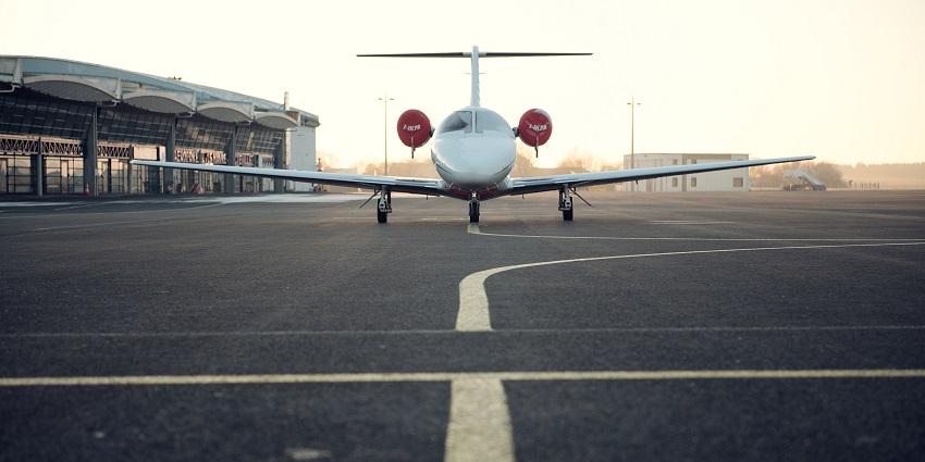 A private jet is stationed on the tarmac as the sun casts a warm glow over the airport.