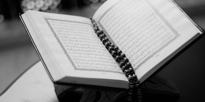 A Book with Arabic script and a beaded chain on a stand, photographed in black and white.