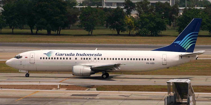 A Boeing aircraft of Garuda stands near a passenger bridge at an airport.