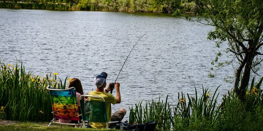 Two people fishing while sitting on an outdoor lounge chair surrounded by lush greenery.