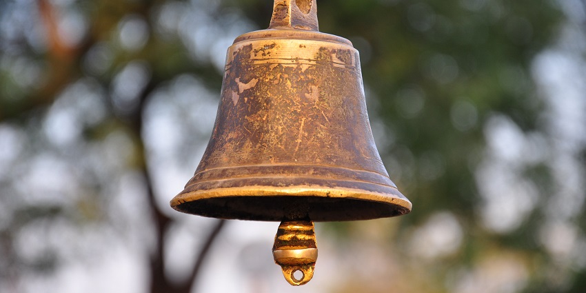 Large ancient metal bell hanging in a temple with intricate carvings on the bell's surface