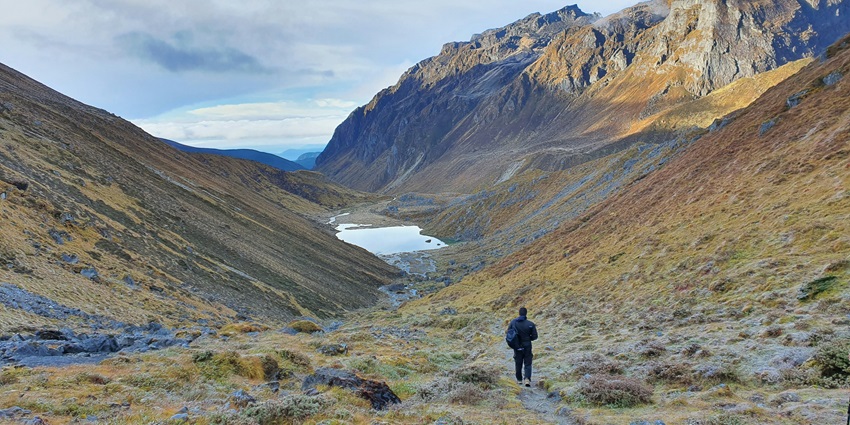 An Indian hiker standing on a ridge with views of Kanchenjunga near Goecha La summit.