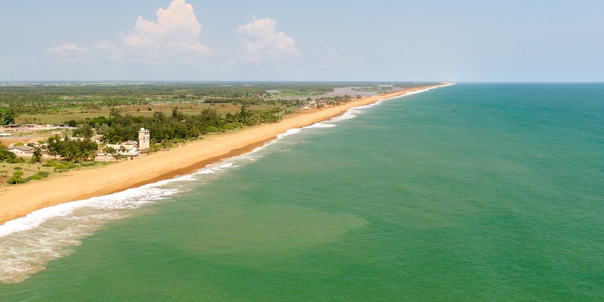 Golden sands of Grand Popo Beach meet the blue ocean under a bright, sunny sky.