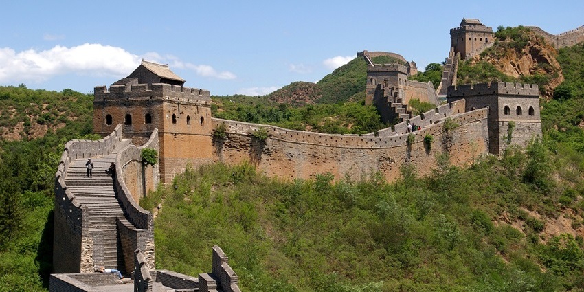 A section of the Great Wall of China extending across green hills under a clear sky.
