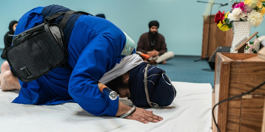Sikh devotees bowing in reverence, inside the gurdwara dressed in traditional Sikh attire.