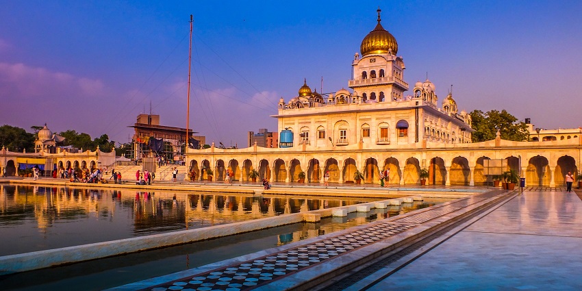 Complex of a gurudwara with a waterbody in the middle and people standing at a distance
