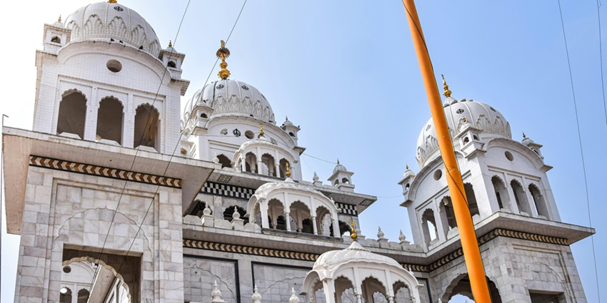 White marble architecture of a gurudwara with gold plated peaks over round tops.