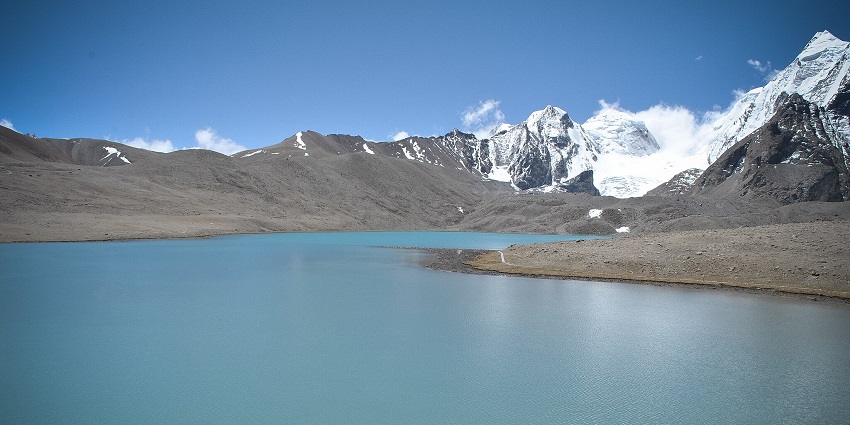 Gurudongmar Lake with a clear water body and Tibetan flags on the surrounding sandy shores