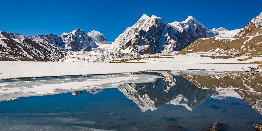 Gurudongmar lake with a small clear water body, snowy shoreline and snowy mountains