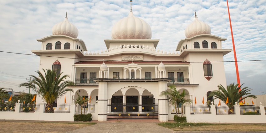 Gurudwara sahib with three white domes on top, multiple flags on the wall and a gate