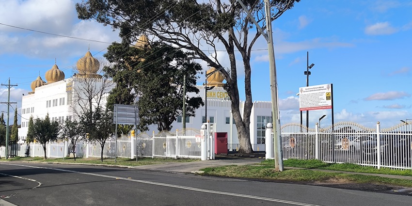 Gurudwara sahib with a distant white architectural building and green trees lined up