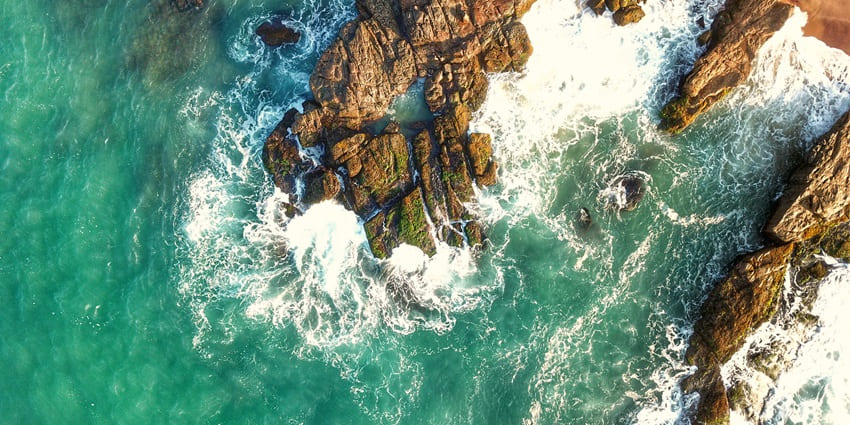 Turquoise-blue water waves hitting rugged rocks at the shores of Hambantota Beach.