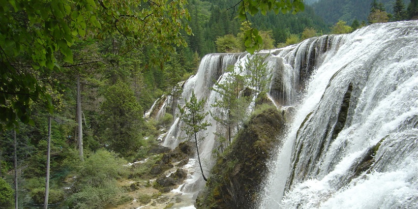 A waterfall similar to Hampi Falls cascading over a rocky terrain, surrounded by greenery